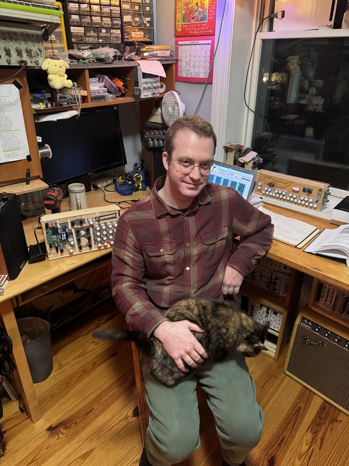 Mason in the studio with a tortoiseshell cat, surrounded by homemade instruments
