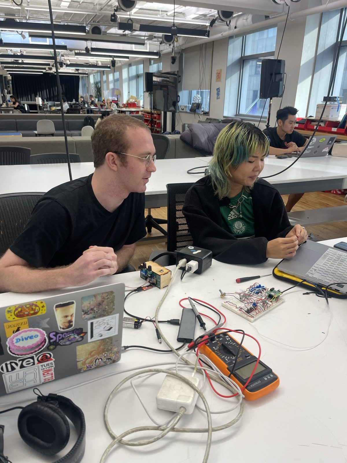 Working at a bench with a breadboard, multimeter, and a collaborator